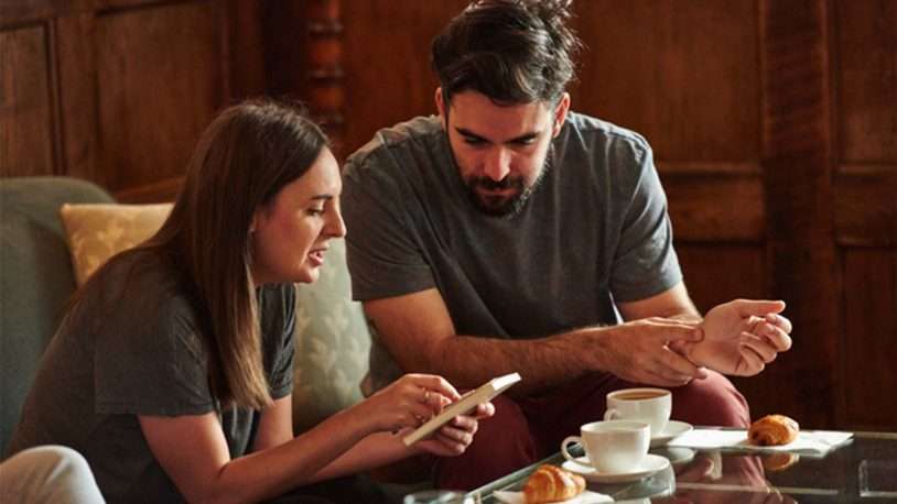 A woman and man sit together at a table with coffee cups and pastries, looking at a tablet device. The cosy setting, ideal for collaboration, suggests they might be discussing strategies for a B2B brand or consulting with a digital agency.