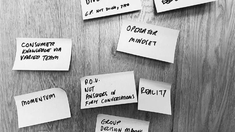 Seven handwritten sticky notes with phrases about business strategies, such as Investment Diversity, Operator Mindset, Momentum, and Reality, are arranged on a wooden surface—providing inspiration for anyone seeking insight from a brand strategy agency.